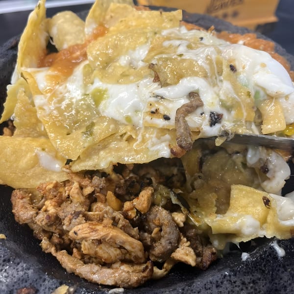 Close-up of La Cantina's nachos with melted cheese, salsa, and meat in a dark bowl.