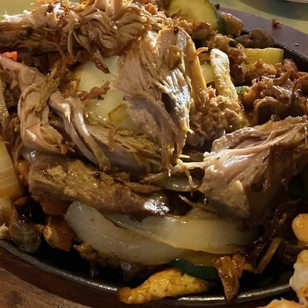 Close-up of a sizzling Mexican fajita platter with shredded meat, onions, and vegetables.
