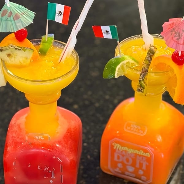 Two colorful La Cantina Mexican Restaurant margaritas in unique bottles, garnished with fruit and Mexican flags.
